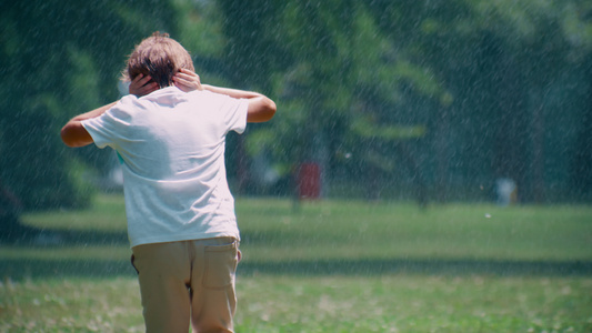 在公园的洒水装置下奔跑的小男孩独自躲着水滴的耳朵视频