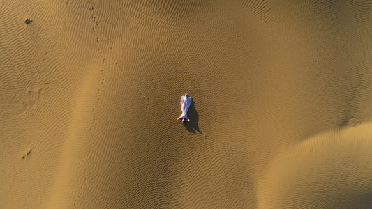 穿着白色连衣裙的年轻女子躺在沙漠的金色沙滩上空中垂直视频