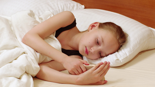 年轻女子看着手机躺在白色的床上十几岁的女孩在白色卧室视频