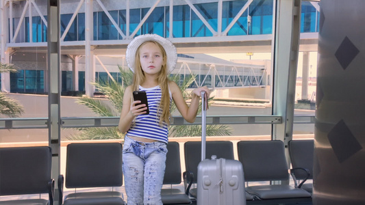 携带移动电话和手提箱在机场出发休息室等候的年轻女青年视频