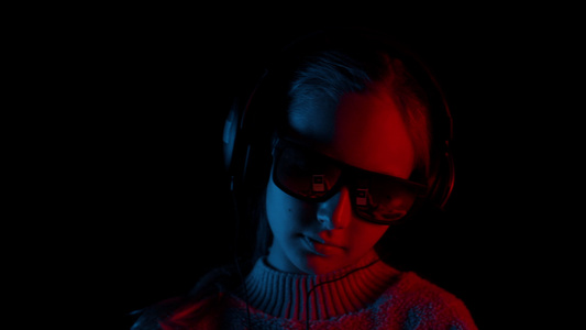 戴着耳机的年轻女孩在黑暗的工作室里用红色和蓝色的灯光视频