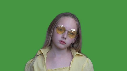 戴着黄色眼镜和穿着绿色背景的相机的年轻女孩严肃的女孩视频