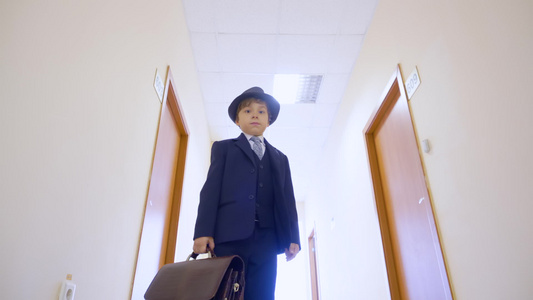 穿着西装的小男孩戴着帽子站在学校走廊里看着镜头低角度视频
