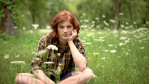 一个年轻的红发小子坐在花园的草坪上长着野花22秒视频