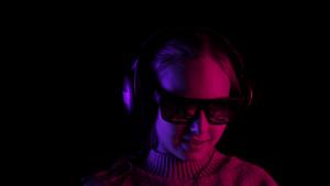 快乐的女孩在带红色和蓝色背光的黑暗工作室的耳机里听8秒视频