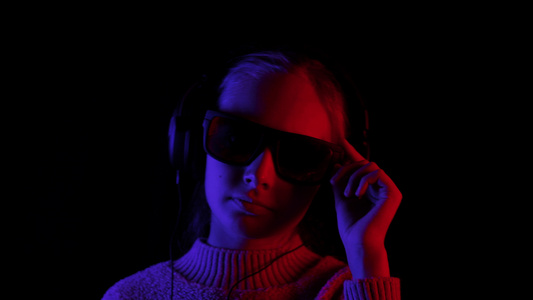 快乐的女孩在耳机和黑色太阳镜在红色和蓝色灯光的黑暗视频