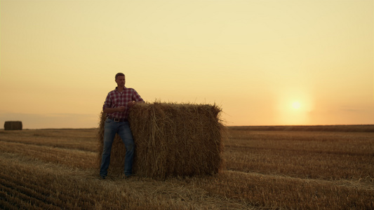 在金色的夕阳下农民独自站在干草堆田里视频
