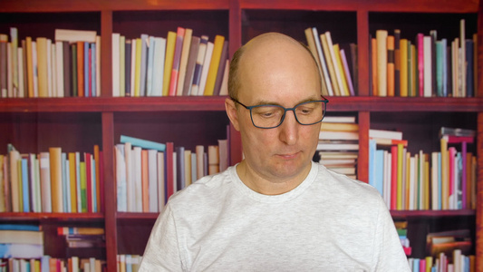 有思想的人在书柜背景上的家庭图书馆看书的眼镜沉思的视频