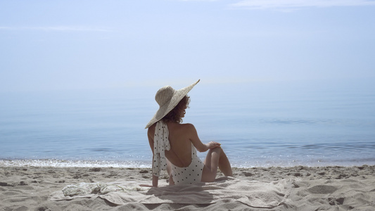 诱人的女人坐在沙滩上穿着泳装在美丽的海浪前视频