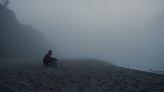 在有雾的早晨坐在海边的沮丧的人视频