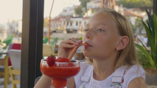 肖像十几岁的女孩在户外夏季咖啡馆用稻草喝草莓鸡尾酒视频