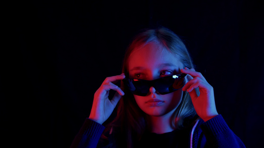 戴着黑色太阳镜的少女在黑暗的房间里四处张望红光和蓝光视频