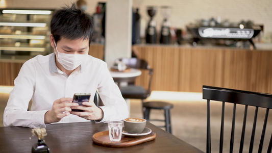 身戴外科口罩的亚裔男子使用智能手机在咖啡店订购饮料视频