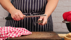 穿蓝色围裙的女人用刀磨厨房刀和手柄在桌子上的利刃12秒视频