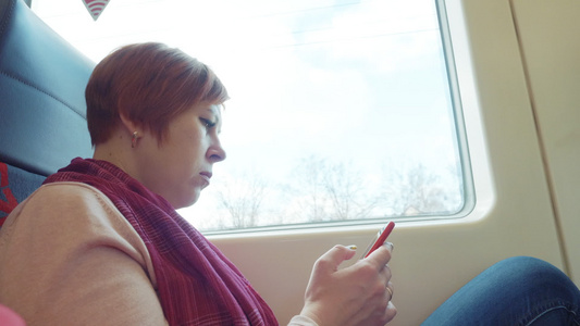 成年成年妇女乘车时使用手机乘坐车身在窗口背景的火车视频