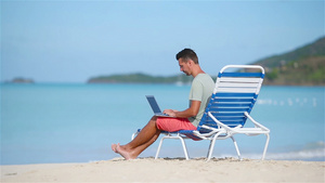 在热带加勒比海滩上携带笔记本电脑的青年男子男人坐在17秒视频