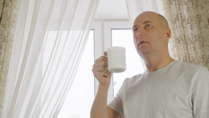 成年男子在窗户背景的舒适厨房里喝早间咖啡肖像开朗的11秒视频