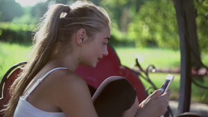 金发女孩坐在公园的长椅上看手机19秒视频