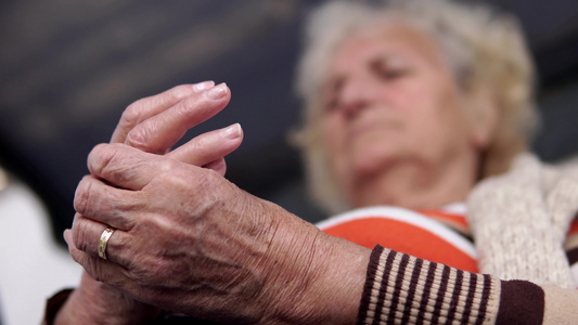 老妇人坐在户外门廊秋千椅上在疼痛的手上做理疗康复按摩疗法视频