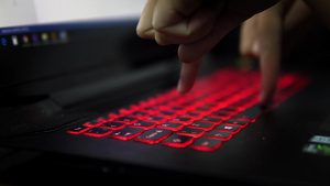 在黑暗中用两个手指在带有红色键盘的笔记本电脑上打字22秒视频