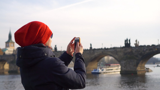 在PragueCharles桥的红帽子女游客与智能手机视频
