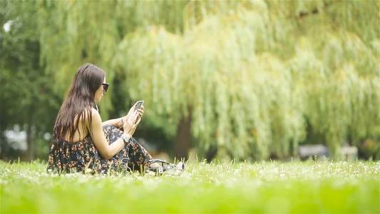 可爱女人坐在公园里时正在看手机短信的短信笑声视频