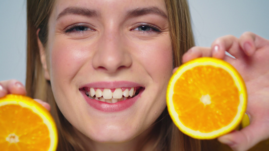 特写镜头：一个积极的女人在工作室里用手拿着橘子做鬼脸视频