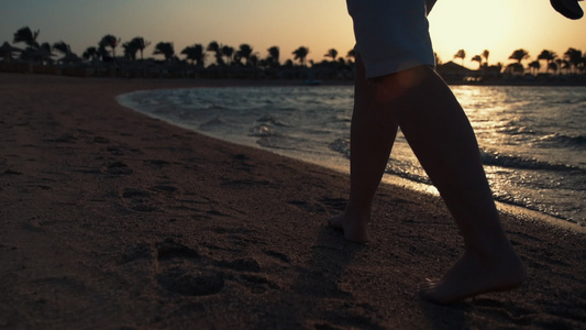 赤脚的年轻女性在沙滩上行走逆光剪影视频
