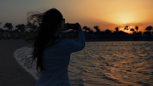 美丽女性在海边手机拍摄日落海景视频