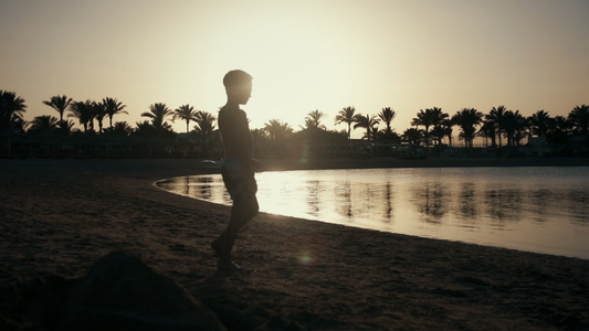 少年男孩在沙滩上行走夕阳逆光剪影视频