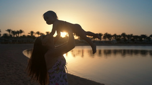快乐的妈妈抱着儿子举高高在海边享受假期逆光剪影22秒视频