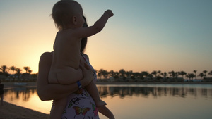 美丽的年轻母亲在日落海滩手抱着小孩逆光13秒视频