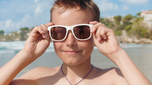 快乐的男孩在海边带着墨镜看着镜头享受夏天视频