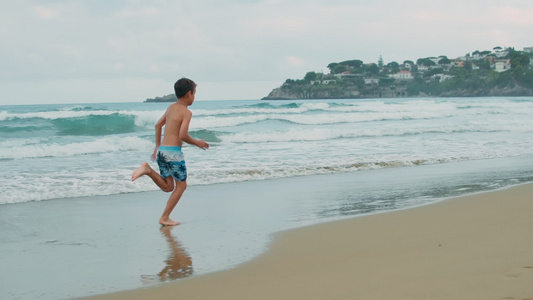 快乐的男孩在海滩上享受暑假沿着海浪奔跑视频