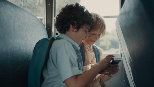 两个学生坐在校车上玩手机游戏视频