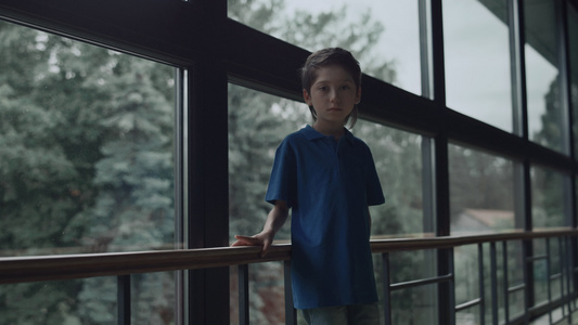 悲伤的男孩独自站在全景窗前视频