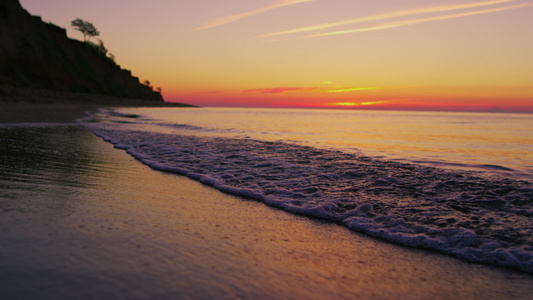 宁静的海洋海岸线与山丘剪影在明亮的橙色日落视频