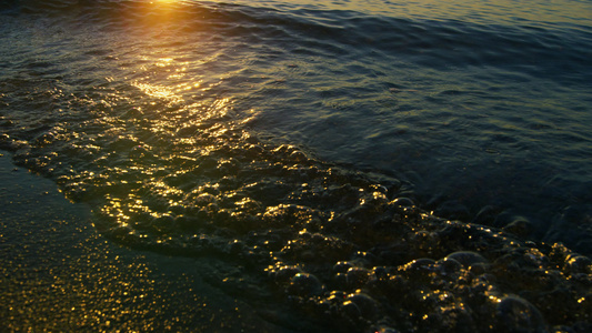 在日出的早晨特写平静的海浪溅起沙滩上的沙子视频