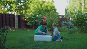 年轻母亲和两个孩子在阳光明媚的日子里在后院拆开大纸箱30秒视频