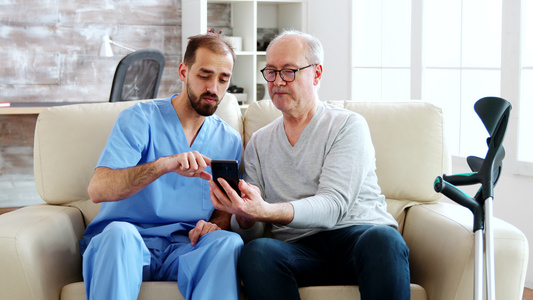 男护士帮助退休老人使用智能手机视频