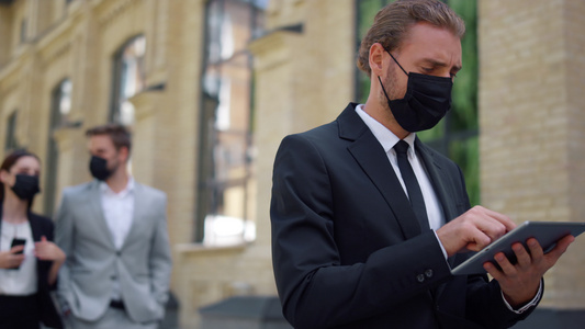 戴面具的商人使用平板室户外工具片 有社交距离的西装男视频