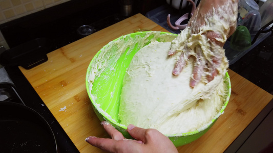 年轻妇女在家里的一个绿色碗里用手揉面包面团人们在家中视频