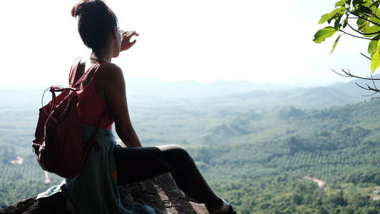一位年轻女子坐在岩石上在阳光明媚的一天旁观背景观看视频