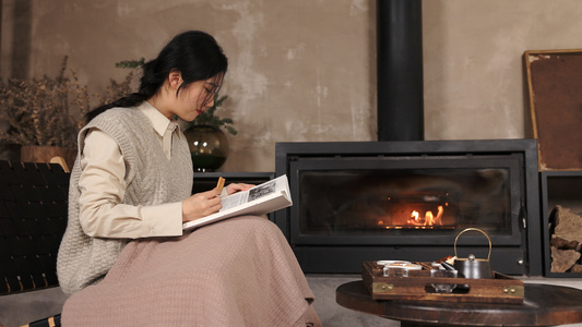 火炉边取暖吃小食看书的女青年视频