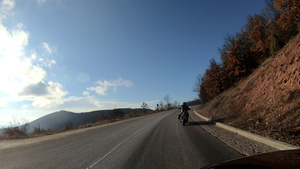 穿着黑色皮夹克的男子在山对面的路上骑着摩托车30秒视频