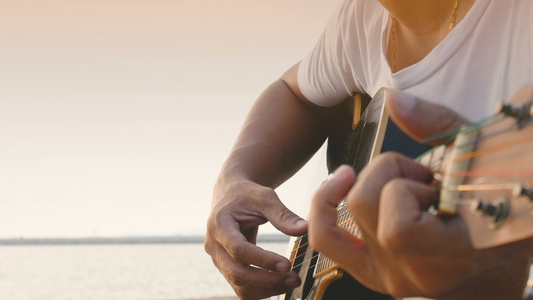 4k日落时关闭一个在海滩弹声吉他的人的近距离让人感到视频