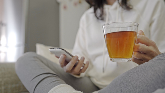 在家照顾自己享受在智能手机上喝茶阅读电子书坐在沙发视频