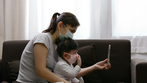 身戴面具的亚裔母亲和女儿拿着电话在视频通话中交谈26秒视频