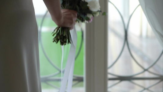 穿着结婚礼服的年轻新娘在室内盛放花束花白色豪华礼服视频