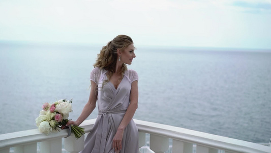 穿着内衣的年轻金发金发女子在露台穿着海观新娘花束视频
